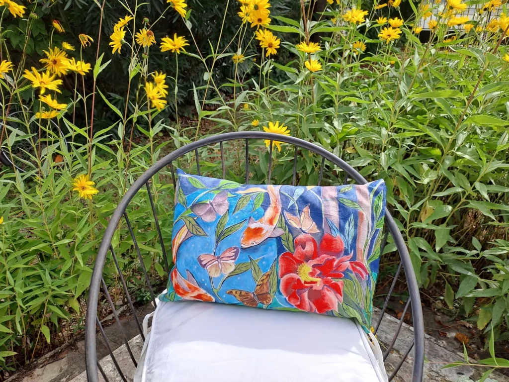 Coussin artisanal bleu avec fleurs, papillons et poissons, photographié dans un jardin