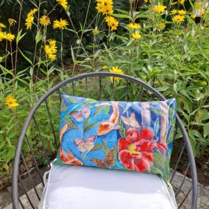 Coussin artisanal bleu avec fleurs, papillons et poissons, photographié dans un jardin